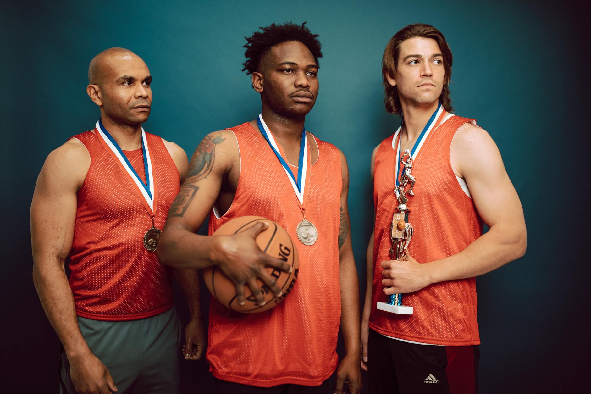 three men wearing medals in orange jersey holding a basketball and trophy